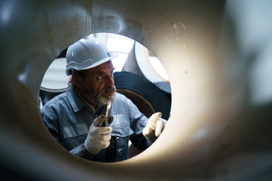 Senior engineer inspects metal sheet coil in factory, quality control concept.