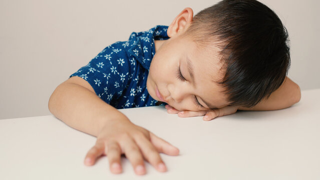 Asian little boy sleeping on a white table, accidentally sleeping without thinking much, on a white background, innocent little boy
