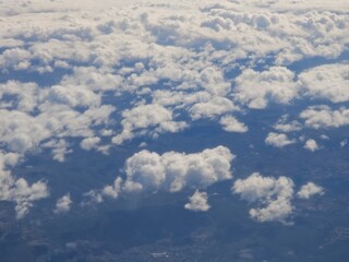 Cloudy sky view from above during daytime flight over landscape with soft white clouds spread over a blue background