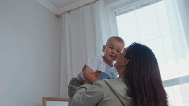 Medium shot shows mother lifting her two year old son high in the air while he smiles and laughs. A playful family moment showing love, emotional wellbeing, and healthy childhood. High quality 4k