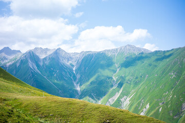 Stunning view of tall green mountains with rugged rocky peaks, rolling grassy slopes, and a bright blue sky with soft white clouds. Perfect scenic background for nature, adventure, and travel themes © pploylp