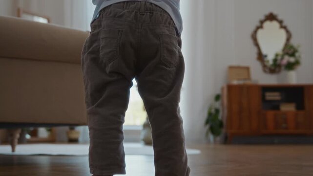 Wide shot shows two year old boy standing up from the floor and making his first steps toward his mother in a bright room. A touching moment of childhood development, joy, and parental support. 4k