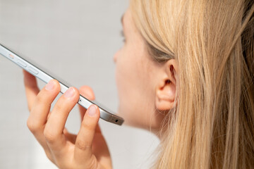 Young blonde woman is listening to voice message by smartphone.