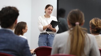 Young female professor explaining subject to classroom full of students - Powered by Adobe