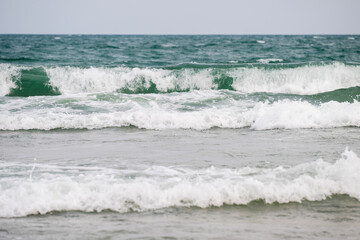 Powerful ocean waves crash onto the shore beneath an overcast sky, capturing the raw energy and...