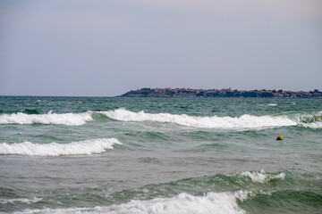 A yellow buoy floats in choppy coastal waters as distant buildings line the misty shoreline under an overcast sky, Bulgaria