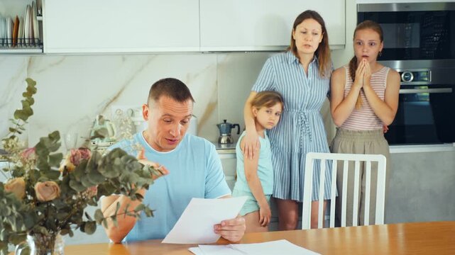 Family quarrel at home kitchen in presence of children. Middle-aged man reads, studies financial document and wife scolds him for signing unreasonable unprofitable contract with bank, lender