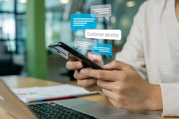 Close-up view of person using smartphone with digital chat bubbles appearing from the screen over a laptop