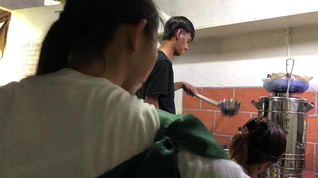 A team of Asian workers is at a small local winery: one is capping bottles, one is scalding bottles, and another is bottling wine.