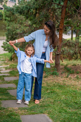 Fototapeta premium Mother and daughter wearing matching striped shirts and jeans while spending time together outdoors. Concept of family bonding, fashion harmony and casual everyday moments.