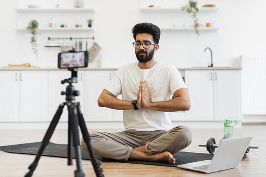Young adult man sitting in modern kitchen recording video blog about fitness and mindfulness while meditating. Promoting healthy lifestyle including mental and physical wellness to his online audience - Powered by Adobe