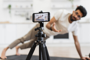 Middle-aged man performs plank exercise while recording fitness video tutorial using smartphone camera setup.
