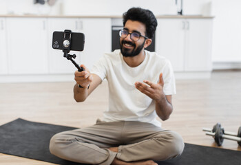 Young adult male explaining fitness and health routines on camera while seated on yoga mat indoors.