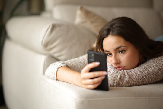 Apathetic woman checking smart phone on a couch at home