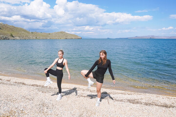 Two women practicing yoga poses on the shore of a tranquil beach during a sunny day
