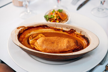 Traditional quenelle de brochet in lobster sauce served in an oval ceramic dish on a white tablecloth. Culinary heritage, French cuisine, sustainable fishing, cultural preservation
