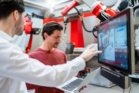 Technician and colleague working together at robot factory