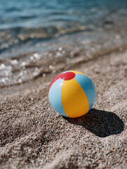 Obraz premium Colorful beach ball on sand near blue sea on sunny day.