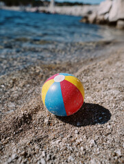 Obraz premium Colorful beach ball on sandy shore by the ocean.