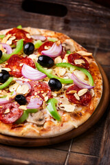 Pizza with chorizo ​​sausage, mozzarella cheese, green pepper and black olives. Rustic wooden background. Soft focus.