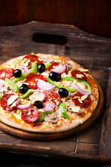 Pizza with chorizo ​​sausage, mozzarella cheese, green pepper and black olives. Rustic wooden background. Soft focus.	