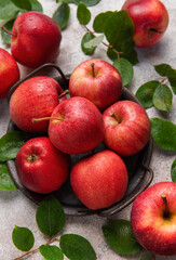 Fresh red apples with green leaves resting in a metal basket