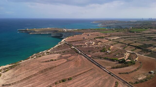 Beautiful aerial view of southern Malta's farmlands and peninsulas bordered by rocky Mediterranean coastline on a summer day.