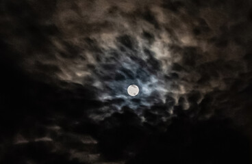 Full moon casting a bright glow over dark, ominous clouds, creating a spooky atmosphere ideal for...