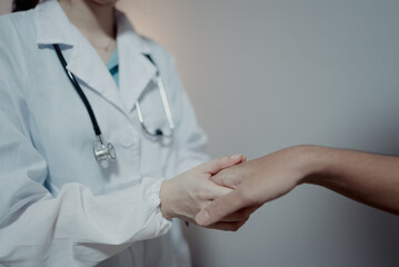 Doctor holding patient’s hand in medical consultation room. Concept of healthcare, compassion,...