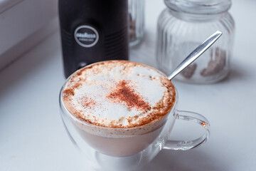 Fresh cappuccino topped with aromatic cinnamon in a clear cup, showcasing foamy texture and creamy layers, perfect for coffee lovers seeking delicious experiences