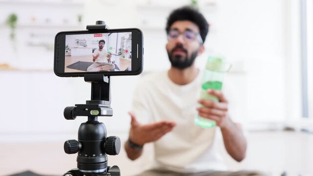 Young man recording health video blog discussing fitness, water consumption, proper hydration, lifestyle tips. Engages digital audience by sharing techniques for better sports practices.