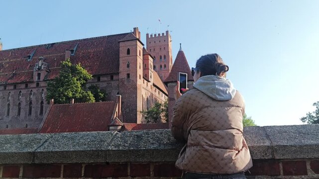 Tourist woman taking photo of Malbork Castle UNESCO heritage site in Poland