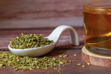 Dried moringa oleifera leaves in a white ceramic spoon and herbal tea infusion on a rustic wooden...
