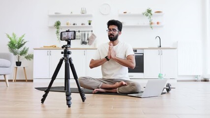 Young adult man sitting in modern kitchen recording video blog about fitness and mindfulness while meditating. Promoting healthy lifestyle including mental and physical wellness to his online audience