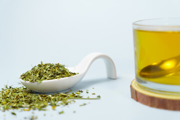 Spoonful of moringa oleifera dried leaves with a glass of herbal tea infusion on a white background...