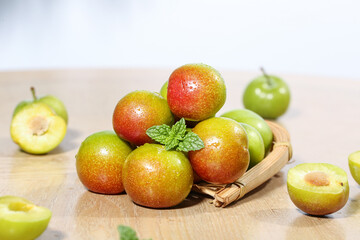 Fresh Red and Green Plums in Wicker Basket with Mint on Wooden Base