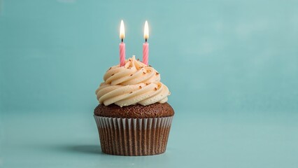 Chocolate cupcake with two pink candles and vanilla frosting on blue background for birthday celebration