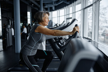 Elderly woman riding an exercise bike in a bustling gym