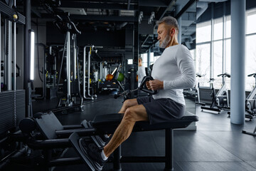 Senior man performs rowing exercise at modern gym