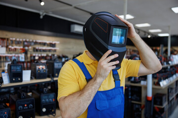 A man in a workwear wearing a protective welding helmet inside a store