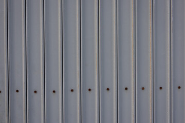close-up, full-frame shot of a gray corrugated metal sheet with a row of rusty bolts.