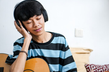 Young Asian Man With Closed Eyes Plays Acoustic Guitar Lost In The Music While Wearing Headphones