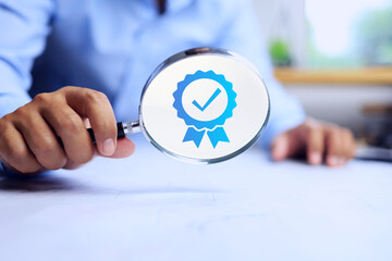 Quality assurance concept where businessman holds a magnifying glass to search for certified...