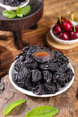 California Air-Dried Prunes in Bowl with Fresh Mint and Cherries on Wooden Table
