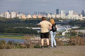 Couple looking on residential buildings standing on a hill on city background, back view. Family leisure, future planning, real estate concept