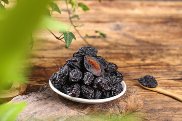 Air-dried Xinjiang prunes in bowl on wooden table with fresh green leaves - healthy organic dried fruit snack