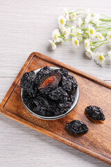 Air-dried prunes in bowl on wooden tray with daisy flowers, Xinjiang candied fruits healthy snack food photography