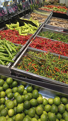 Fresh market display of assorted chili pepper and lime produce in metal bins with vivid color contrast and lively atmosphere