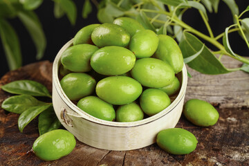 Fresh Green Olives in Wooden Bowl with Olive Branch on Rustic Wood Table