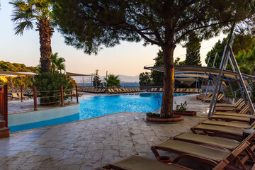 Tranquil holiday scene with a luxury swimming pool surrounded by sun loungers, palm trees, and summer greenery. Perfect for travel, vacation, relaxation, tourism, hotels, resorts, and summer lifestyle